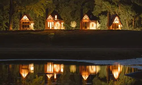 Quattro baite illuminate di notte, riflesse nell'acqua