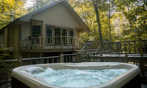 Una vasca idromassaggio con gorgogliatori davanti a una baita tra gli alberi