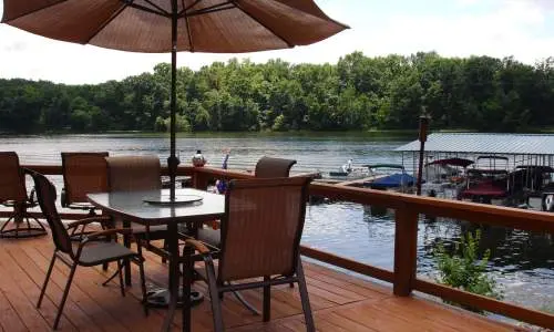 Una terrazza con sedie e ombrellone che si affaccia su un lago con barche attraccate nelle vicinanze