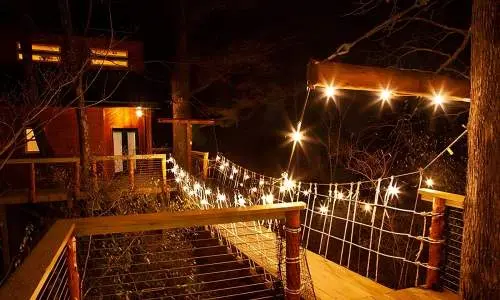 Un ponte di legno che conduce a una casetta sull'albero illuminata da luci a corda