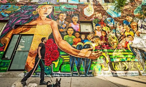 Un uomo che porta a spasso tre cani davanti a un murale colorato.