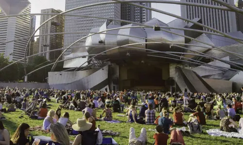 Centinaia di persone sedute su tappeti da picnic davanti al Pritzker Pavillion 