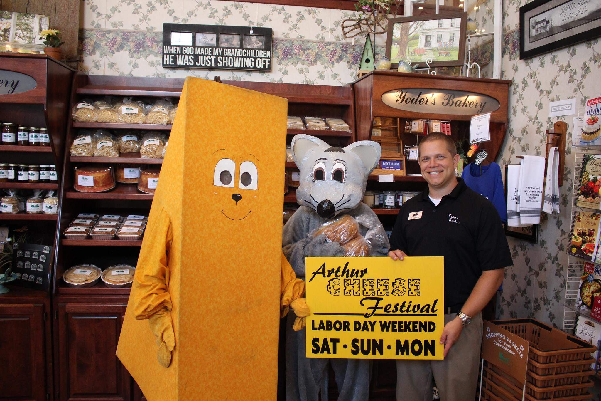 Mascotte in costume da formaggio e da topo in piedi accanto a un uomo che regge un cartello dell'Arthur Cheese Festival