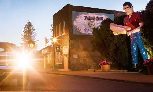 Tramonto dietro un'auto con una statua gigante di un uomo con in mano un hotdog