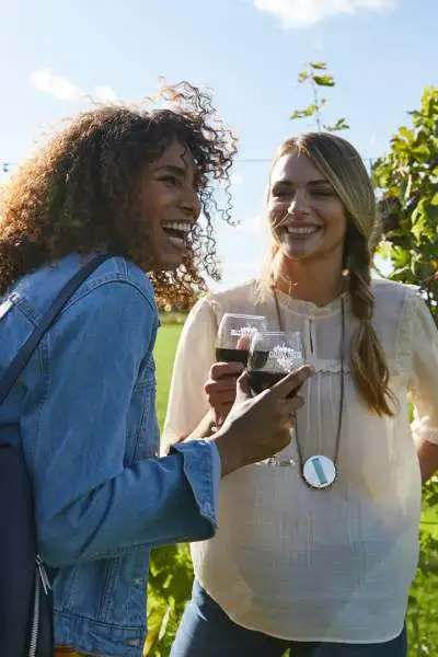 Due ragazze ridono gustando vino rosso in un vigneto