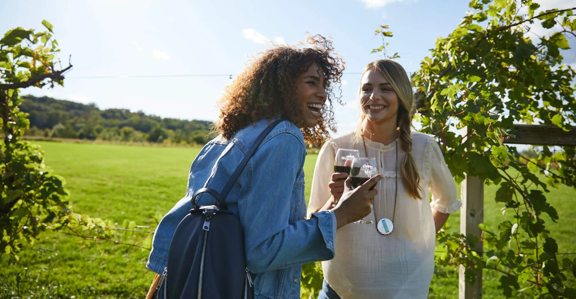 Due ragazze ridono gustando vino rosso in un vigneto