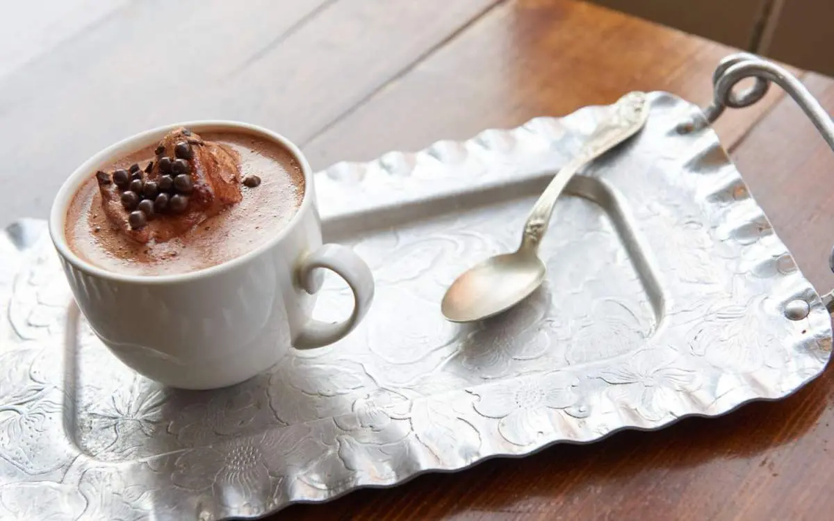Una tazza di cioccolata calda e un cucchiaino appoggiati su un vassoio da portata.