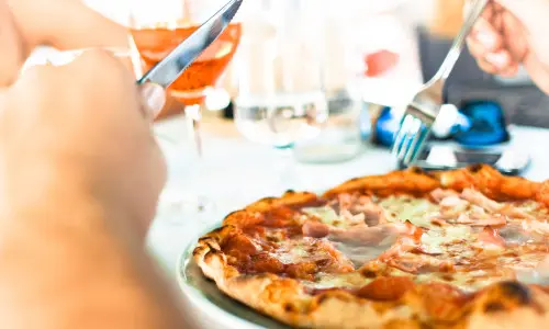 Persona che mangia la pizza con coltello e forchetta