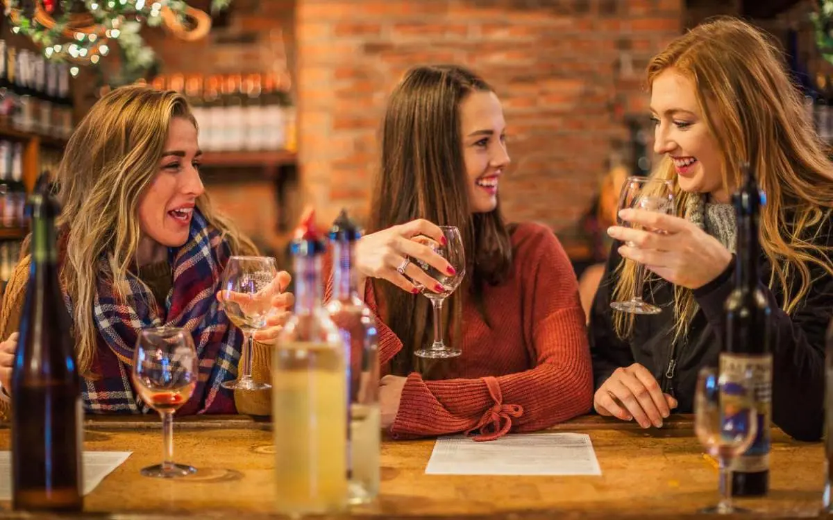 Tre donne sedute a un tavolo che gustano un bicchiere di vino all'interno di una cantina