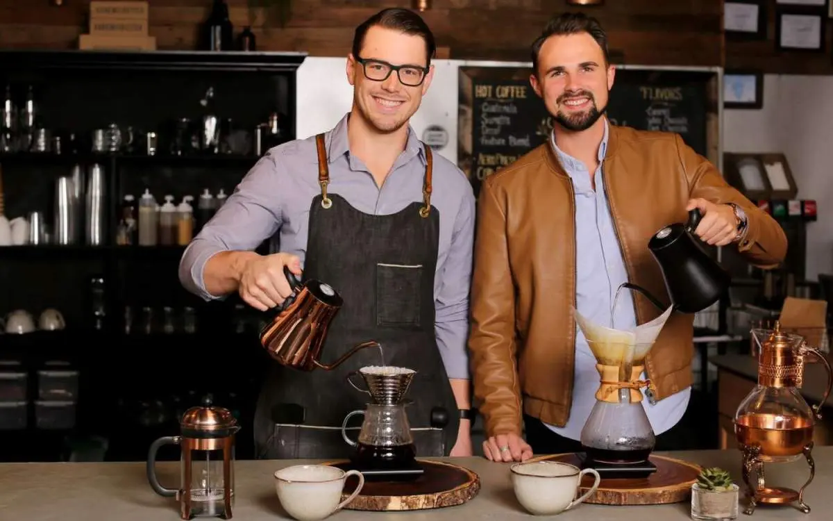 Due uomini guardano la telecamera mentre versano un caffè filtro in un bar