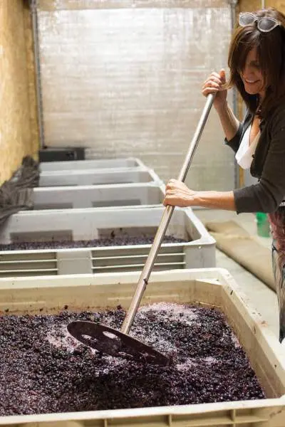 Una donna che mescola l'uva in un grande contenitore per fare il vino.