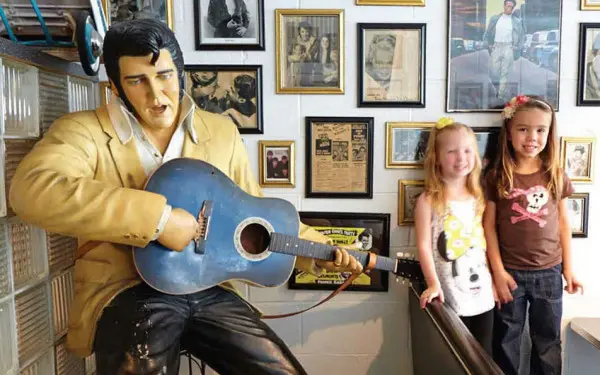 Due ragazzini si fanno fotografare accanto alla statua di Elvis Presley con in mano una chitarra