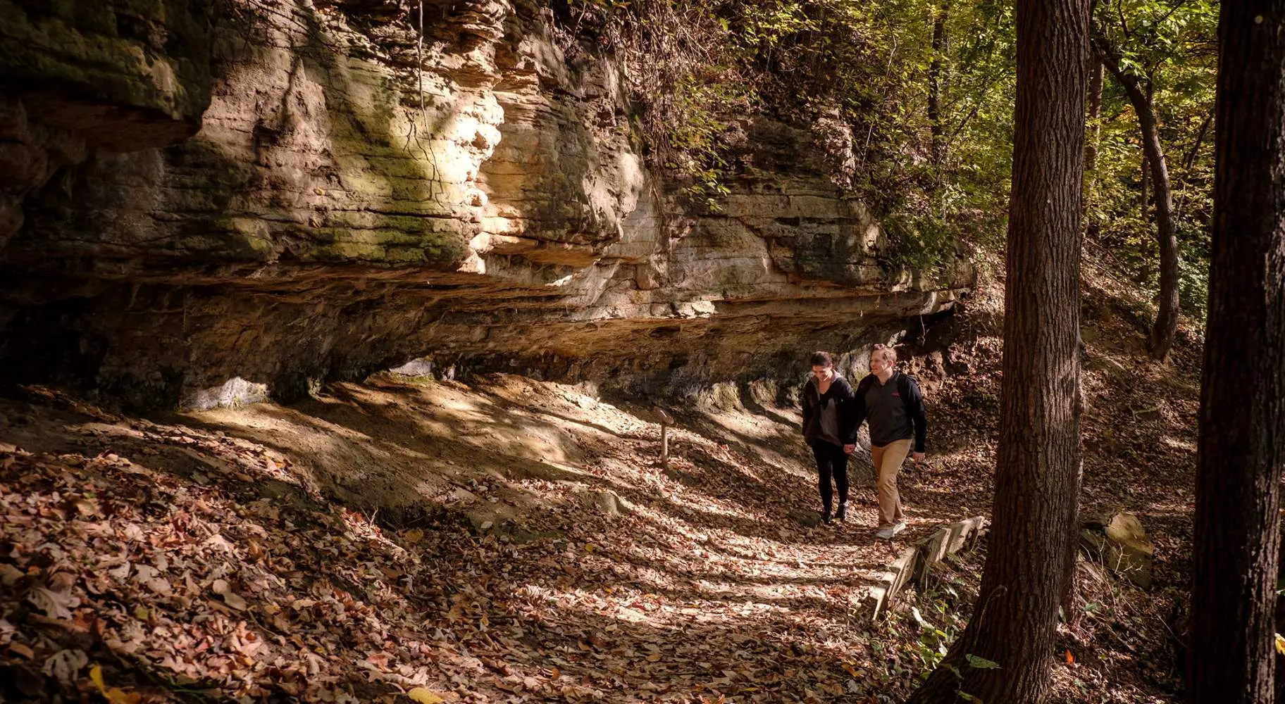 Due persone che camminano nella foresta lungo una grande roccia