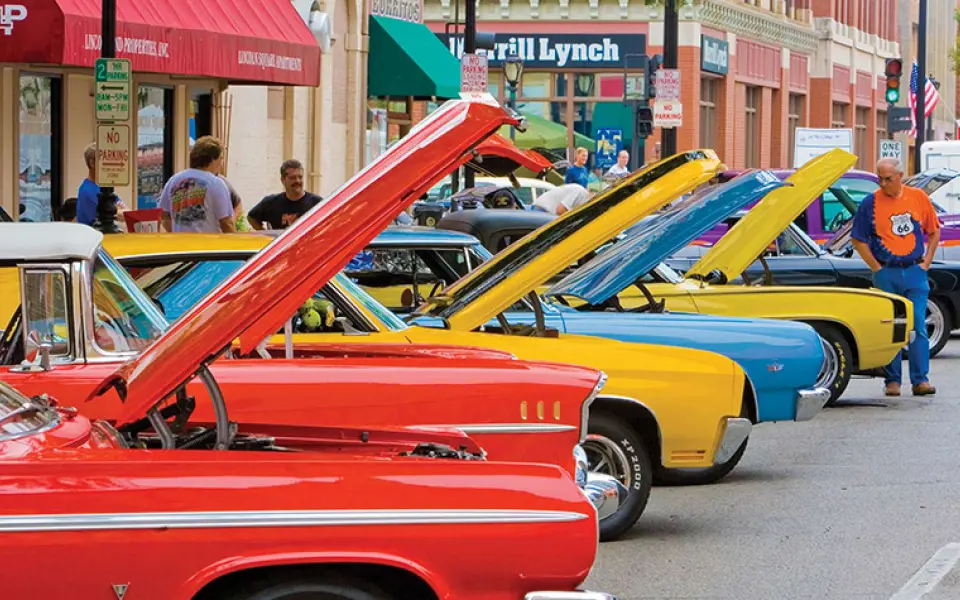 Auto d'epoca dai colori vivaci, con il cofano sollevato, sono allineate lungo una strada del centro in occasione di un raduno automobilistico sulla Route 66.