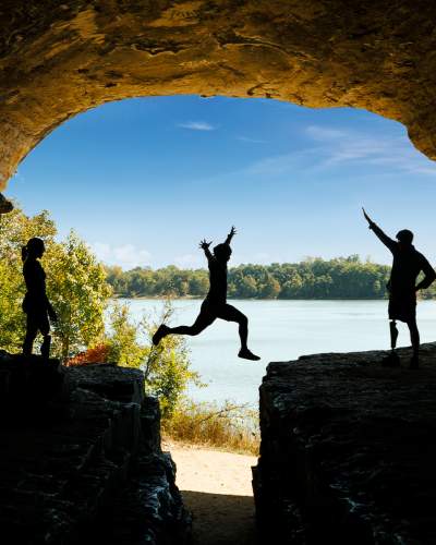 Una persona salta su una roccia con gli amici, il cielo azzurro e l'acqua sullo sfondo