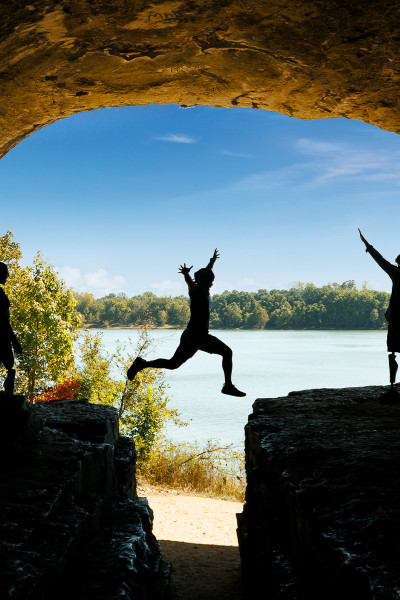 Una persona salta su una roccia con gli amici, il cielo azzurro e l'acqua sullo sfondo