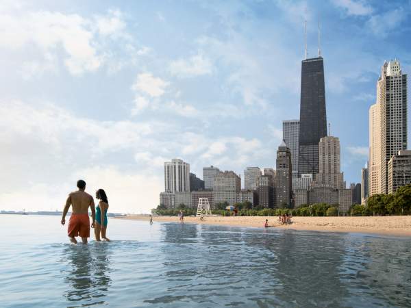 Una coppia che cammina tra le secche del lago Michigan accanto a una riva sabbiosa, con i grattacieli sullo sfondo