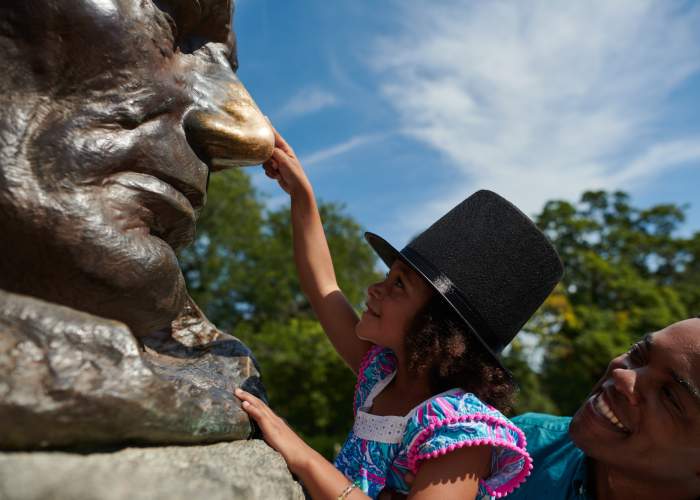 Padre che alza la figlia per toccare il naso della statua di Lincoln.