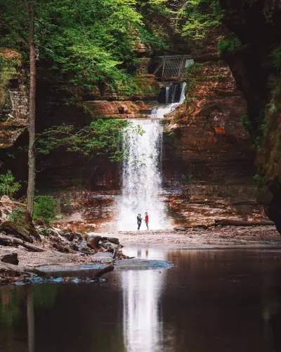 Due persone in piedi davanti a una cascata, accanto a un laghetto sereno.