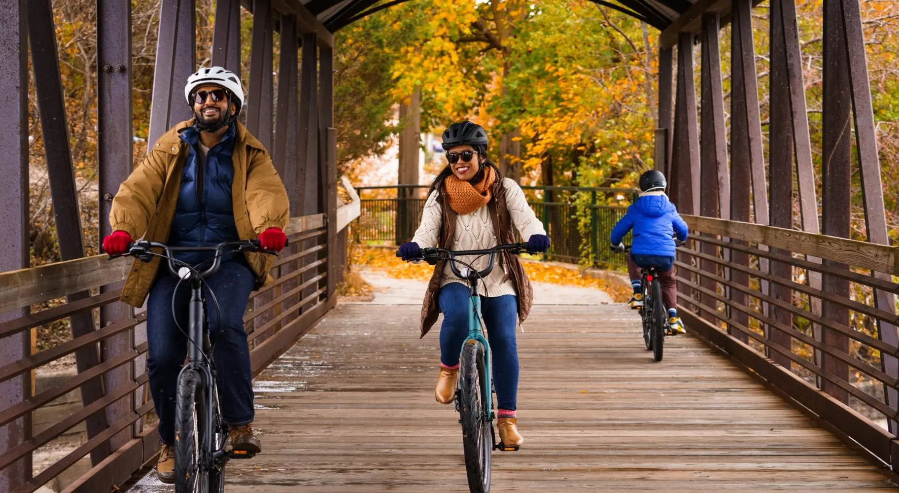 Una coppia in bicicletta su un vecchio ponte coperto in legno, con il fogliame autunnale alle spalle