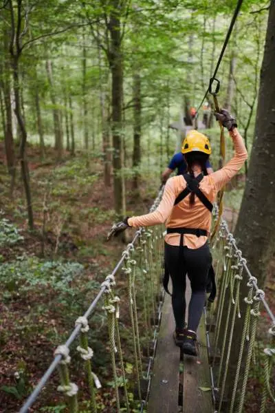 Persone su un ponte che attraversano le foreste con imbracature e caschi di sicurezza al Canopy Tours.