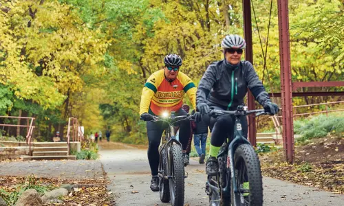 Due ciclisti che percorrono un sentiero boscoso sotto un vecchio ponte di legno