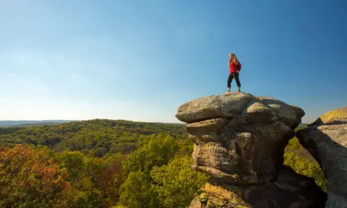 Escursionista in cima a una grande roccia con vista sulla foresta.