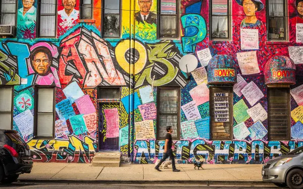 Una persona con un cane che cammina davanti a un murale della cultura messicana