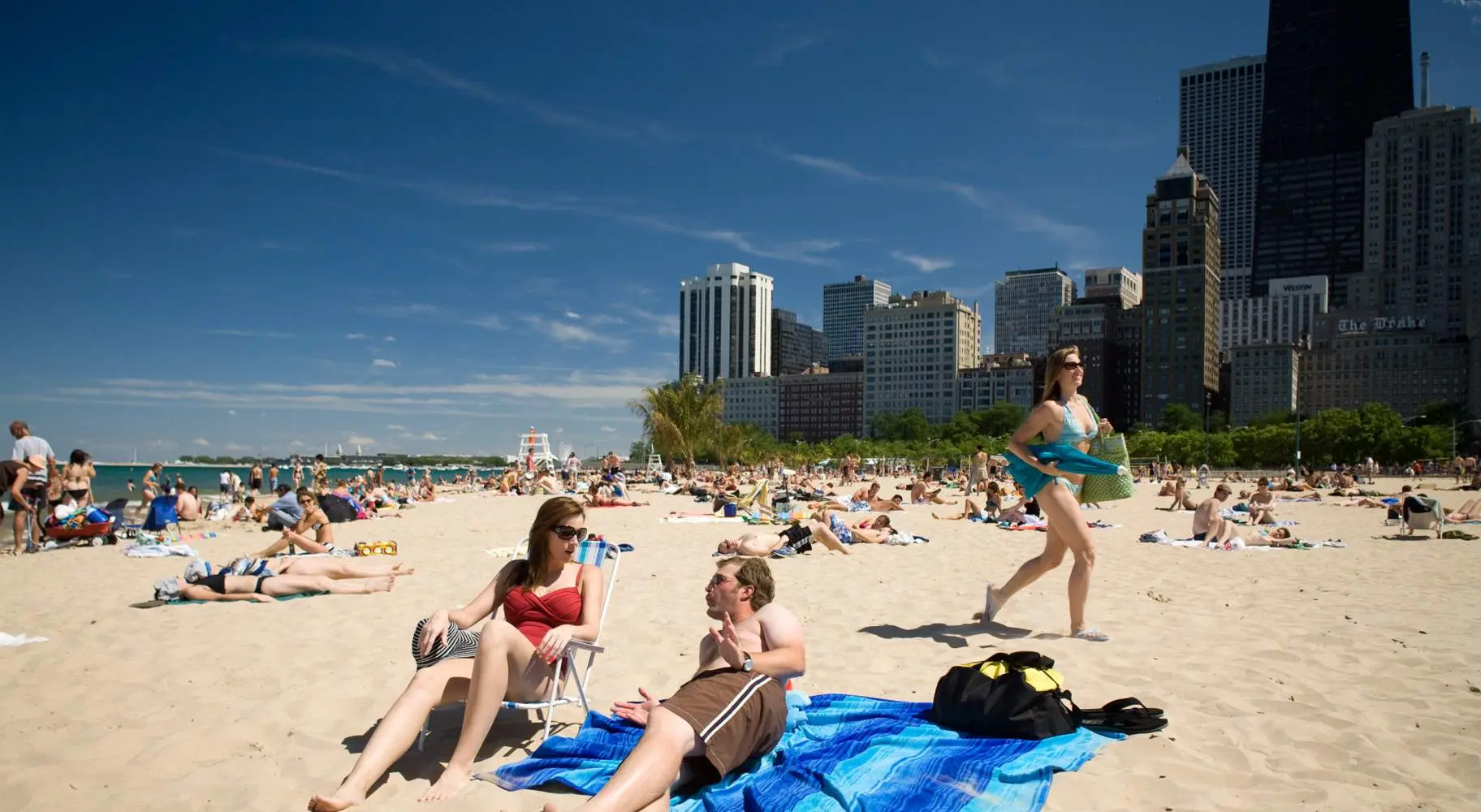 Due persone sdraiate su una spiaggia sabbiosa, con la folla sullo sfondo, insieme allo skyline di Chicago