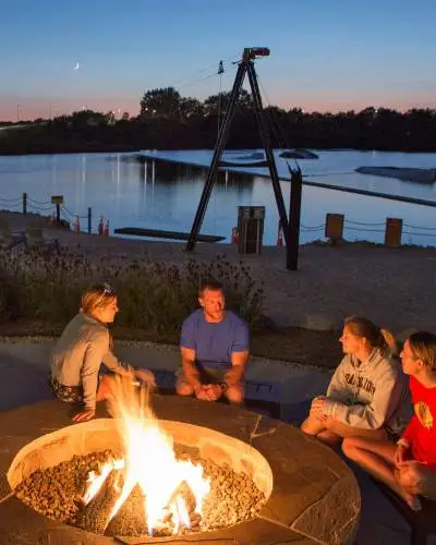 Quattro persone sedute intorno a un fuoco vicino a una spiaggia lacustre al tramonto