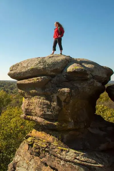 Donna in piedi su una grande roccia che domina la foresta sottostante