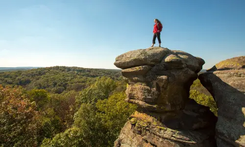 Donna in piedi su una grande roccia che domina la foresta sottostante