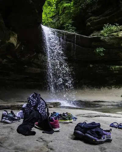 Una cascata da una roccia, con borse e scarpe della gente che giacciono sulla roccia sottostante