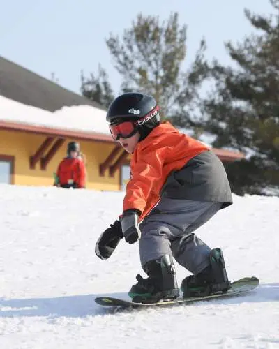 Un bambino in sella a uno snowboard sulla neve, con casco, occhiali e abbigliamento caldo da sci