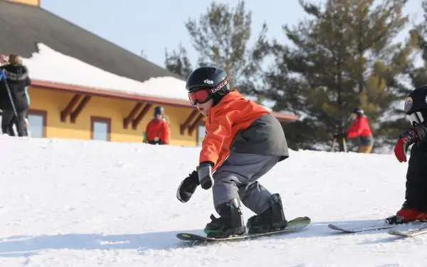 Un bambino in sella a uno snowboard sulla neve, con casco, occhiali e abbigliamento caldo da sci