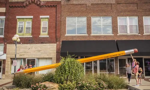 Attrazione gigante a forma di matita con famiglie intorno.