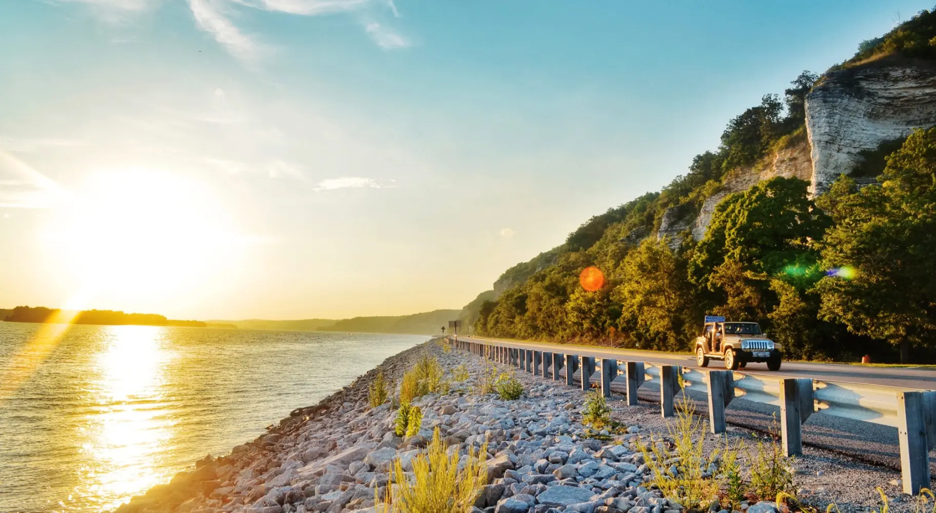 L'alba che splende sull'acqua e un'auto che percorre la strada accanto ad essa