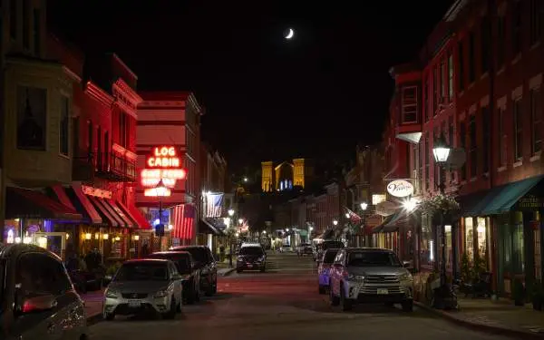 La strada principale di una piccola città di notte, con auto su entrambi i lati della strada e un'insegna luminosa al neon con la scritta "Log Cabin".