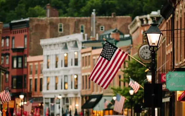 Una bandiera americana appesa alla facciata di un edificio in una strada principale di una piccola città piena di edifici in mattoni