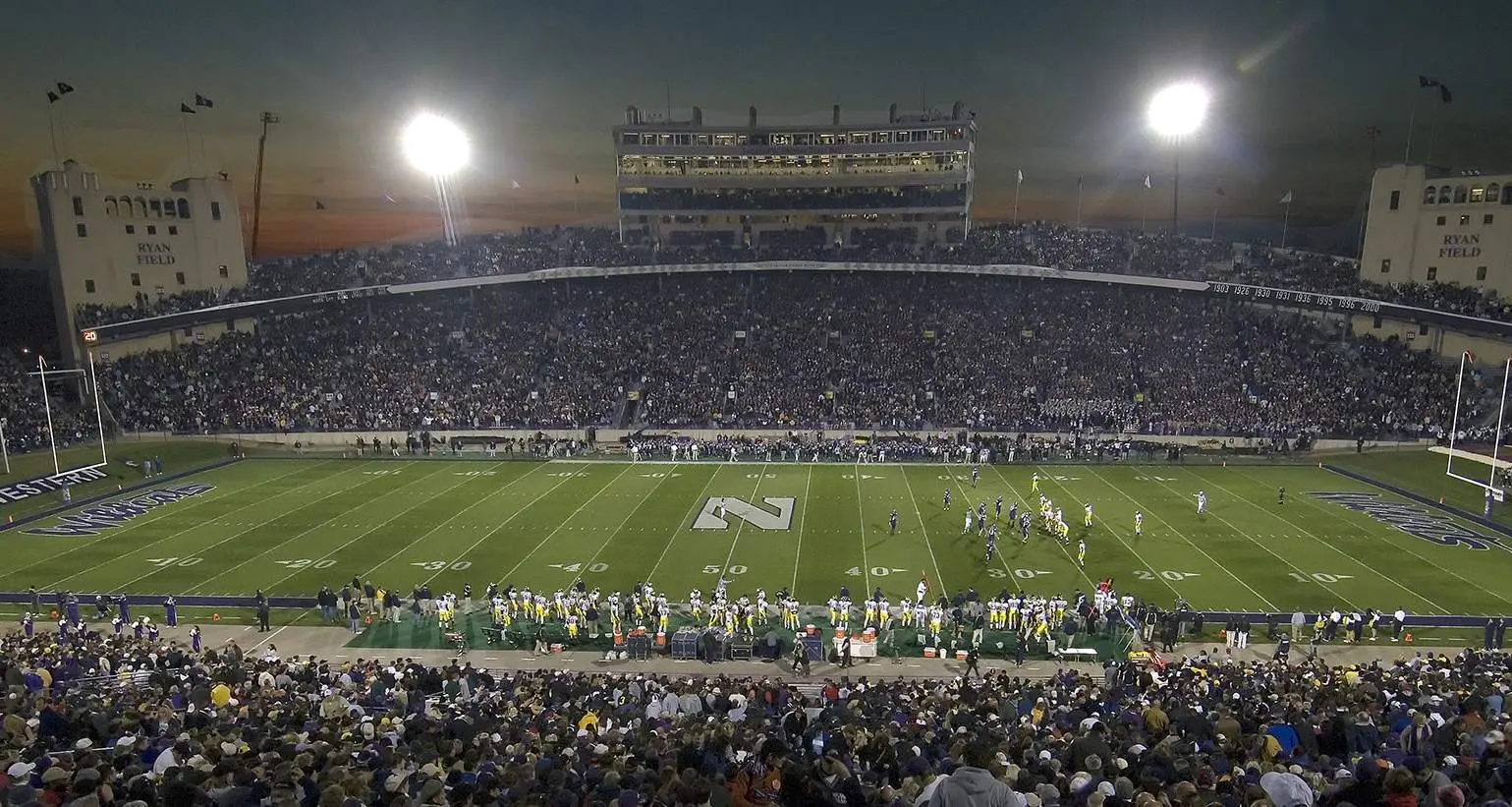 Un grande stadio di football universitario di notte prima di una partita, con gli spalti pieni di spettatori
