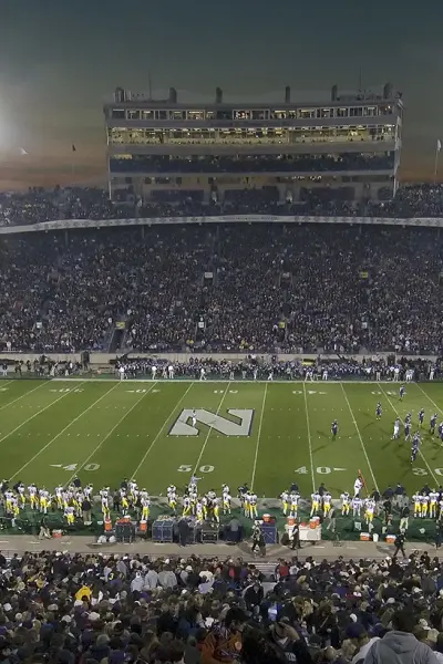 Un grande stadio di football universitario di notte prima di una partita, con gli spalti pieni di spettatori