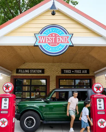 Padre e figlio passano davanti a un SUV verde e a delle pompe di benzina d’epoca alla stazione di servizio West End sulla Route 66.