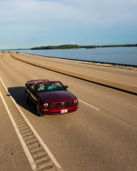 Una decappottabile rossa che percorre una strada panoramica lungo il fiume Mississippi.